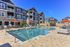 Modern apartment complex with stylish stone and siding exterior, featuring a sparkling swimming pool surrounded by chic lounge chairs and vibrant orange umbrellas.