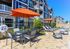 Luxurious apartment complex with a sunlit patio, elegant lounge chairs, vibrant orange umbrellas, and beautifully landscaped surroundings.