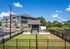 Charming modern apartment complex with manicured lawns, secure fencing, and surrounded by lush greenery under a clear blue sky.