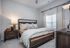 Elegant bedroom with plush bedding, stylish wooden furniture, and ample natural light through a large window with soft drapes.