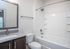 Sleek modern bathroom showcasing a spacious bathtub with tile surround, elegant granite countertop, and a large mirror for a touch of luxury.