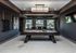Elegant apartment recreation room featuring a sleek pool table, modern decor, and large windows for natural light.