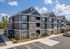 Contemporary three-story apartment building with modern stone facade, ample parking, and lush landscaping under clear blue skies.