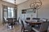 Elegant dining area with modern lighting, round wooden table, and stylish upholstered chairs, enhanced by large windows and sleek cabinetry.
