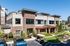 Modern two-story building with elegant brick facade, large windows, and lush landscaping in a sunny urban setting.