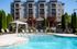 Luxurious apartment complex with a lush poolside area, featuring sun loungers, a stylish gazebo, and vibrant greenery against a modern building backdrop.