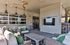 Inviting outdoor patio area with stylish wicker seating, vibrant green cushions, a modern ceiling fan, and a large mounted TV for a relaxing entertainment space.