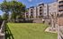Elegant apartment complex with beautifully landscaped green lawn, mature trees, and cozy outdoor seating area, perfect for relaxation and leisure.
