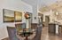 Elegant dining area with a glass-top table, plush chairs, and vibrant floral decor, seamlessly leading into a modern kitchen with sleek cabinetry and stainless steel appliances.