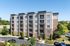 Modern apartment building with five levels, featuring spacious balconies and surrounded by lush greenery and ample parking.