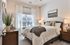 Inviting bedroom with a plush bed, cozy knit throw, stylish decor on a wooden dresser, and abundant natural light through large windows.