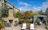 Charming outdoor area with stone fireplace, elegant patio seating, and a cozy gazebo surrounded by lush greenery under a brilliant blue sky.