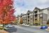 Elegant apartment complex with modern architecture, surrounded by vibrant autumn foliage and ample parking space.