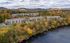 Scenic aerial view of a charming apartment complex surrounded by vibrant autumn foliage and a tranquil river, with picturesque mountains in the background.