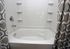 Elegant bathroom featuring a pristine white bathtub with tiled walls and stylish gray patterned shower curtains.
