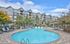 Inviting apartment complex with a sparkling swimming pool, ample lounge seating, and lush landscaping against a bright blue sky.