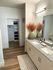 Modern bathroom with dual sinks, elegant granite countertop, and stylish decor, leading to a spacious walk-in closet with wooden flooring.