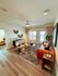 Inviting living room with stylish decor, featuring a modern ceiling fan, cozy seating, and a vibrant geometric rug, leading to a sunlit bedroom.