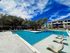 Inviting apartment complex pool area with crystal-clear water, modern lounge chairs, and lush green surroundings under a vibrant blue sky.
