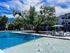 Inviting outdoor pool area with sun loungers and shaded seating, surrounded by lush trees and modern apartments.
