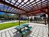 Inviting outdoor space with a shaded pergola, green picnic table, and view of the sunlit lawn area in a modern apartment community.
