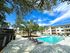 Luxurious apartment complex showcasing a sparkling pool, modern poolside loungers, lush greenery, and stylish multi-level buildings under a bright blue sky.