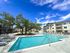 Luxurious apartment complex featuring a sparkling swimming pool with sun loungers and lush greenery under a vibrant blue sky.