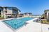 Luxurious apartment complex with a serene swimming pool, stylish poolside seating, and modern architecture set against a clear blue sky.