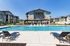 Luxurious apartment complex featuring a stunning outdoor pool area with modern lounge chairs, surrounded by elegant stone buildings under a clear blue sky.