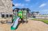 Charming residential complex with a vibrant children's playground, surrounded by modern stone and wood-clad apartment buildings under a clear blue sky.