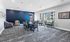 Modern communal meeting room with elegant seating, vibrant blue accent wall, and expansive windows offering natural light.