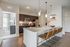 Modern kitchen with granite countertops and sleek pendant lighting, featuring a breakfast bar with stylish seating, opening into a bright living area.