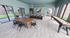 Bright and spacious entertainment room with sleek wooden floors, modern bar seating, a stylish dining area, and a fun shuffleboard table.