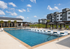 Modern apartment complex with luxurious outdoor pool, surrounded by lush greenery and stylish seating areas.