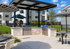 Elegant outdoor barbecue area with sleek stainless steel grills and stylish seating, set against a backdrop of modern apartment buildings and lush green lawn.