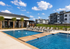 Luxurious apartment complex with a sparkling outdoor pool, surrounded by stylish lounge chairs under a bright blue sky, offering a perfect relaxation spot.