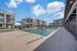 Modern apartment complex with a luxurious swimming pool, surrounded by stylish buildings under a clear blue sky.
