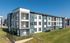 Modern apartment complex exterior showcasing sleek architecture, spacious balconies, and vibrant green surroundings on a sunny day.