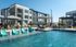 Luxurious apartment complex with modern architecture, featuring a refreshing pool area with stylish lounge chairs and shaded seating.