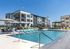 Vibrant apartment complex with a sparkling outdoor pool, sleek lounge chairs, and modern architecture under a clear blue sky.