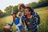 Happy family enjoying a sunny day outdoors, parents giving piggyback rides to kids in a lush green field.