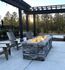 Inviting outdoor patio featuring a modern stone fire pit, surrounded by cozy wooden chairs and a stylish pergola, set against a serene forest backdrop.
