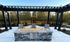Inviting outdoor patio featuring a modern stone fire pit under a stylish pergola, set against a scenic wooded backdrop.