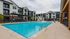 Luxurious apartment complex featuring a sparkling swimming pool with ample seating, surrounded by modern, multi-story buildings.
