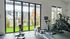 Bright and airy gym room with state-of-the-art exercise equipment, showcasing stunning views of modern apartments and lush greenery through large glass doors.