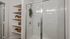 Elegant bathroom with a modern glass-enclosed shower, sleek white tiles, and stylish built-in shelves with decorative plants and wicker baskets.
