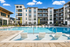 Luxurious apartment complex with a stunning outdoor pool area, surrounded by modern balconies and lush landscaping.