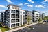 Modern apartment complex with spacious balconies, lush landscaping, and ample parking under a clear blue sky.
