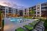 Modern apartment complex with a luxurious swimming pool area, surrounded by stylish green loungers and beautifully landscaped gardens, under a serene evening sky.