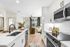 Bright and modern kitchen with sleek cabinetry, stainless steel appliances, and inviting living area. Large windows illuminate the open space, creating a warm and welcoming atmosphere.